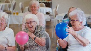 Older adults and children sit together at a table making colorful crafts in a bright activity room.